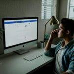 man in blue denim jacket facing turned on monitor